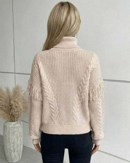 Back view of a woman wearing the Lauven Vienna Sweater, a beige cable knit turtleneck with fringe sleeves.
