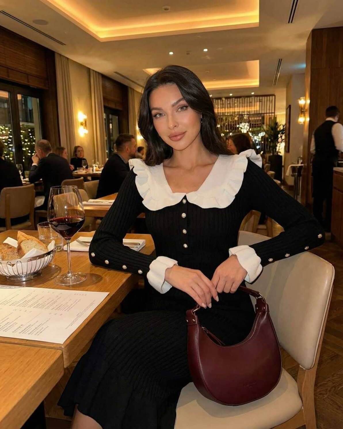 Model wearing Valencia Midi Dress by Lauven with ruffled collar in a restaurant setting.