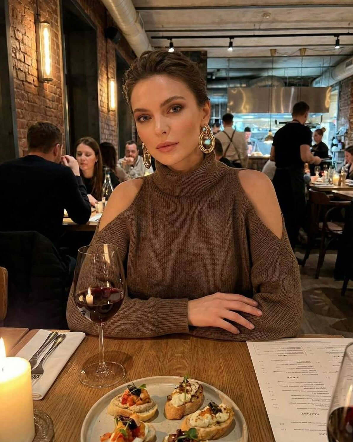 Model wearing Sahara Sweater by Lauven, showcasing cutout shoulders and elegant style at a restaurant dinner.
