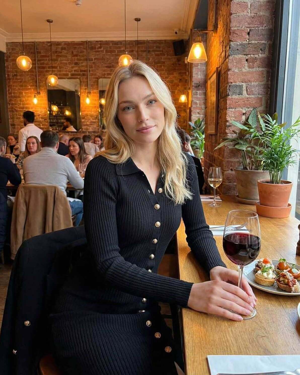 Monaco Midi Dress by Lauven worn by a smiling woman in a restaurant with wine and food, showcasing gold button details.