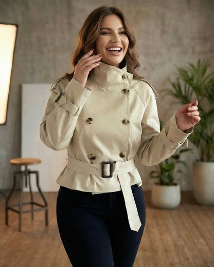 Savona Jacket by Lauven – Women's beige double breasted belted peplum trench jacket in a stylish indoor setting.