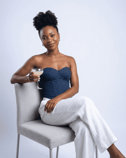 Model wearing the Atlas Corset Top by SLIMONA, a navy faux denim bustier, sitting with a cocktail.