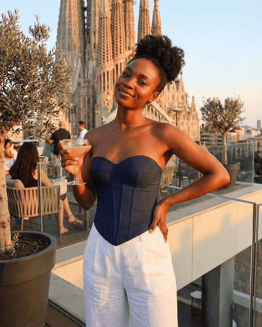 Model wearing Atlas Corset Top by SLIMONA, posing with a cocktail against a scenic rooftop backdrop.