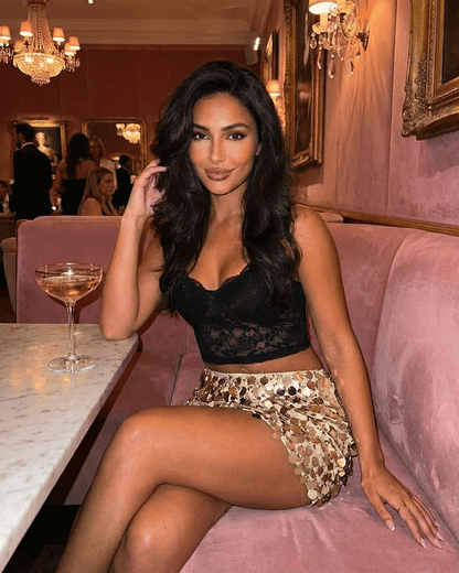 Aurelia Mini Skirt by SLIMONA worn by a woman sitting in a stylish setting, showcasing gold sequin hem and bodycon fit.
