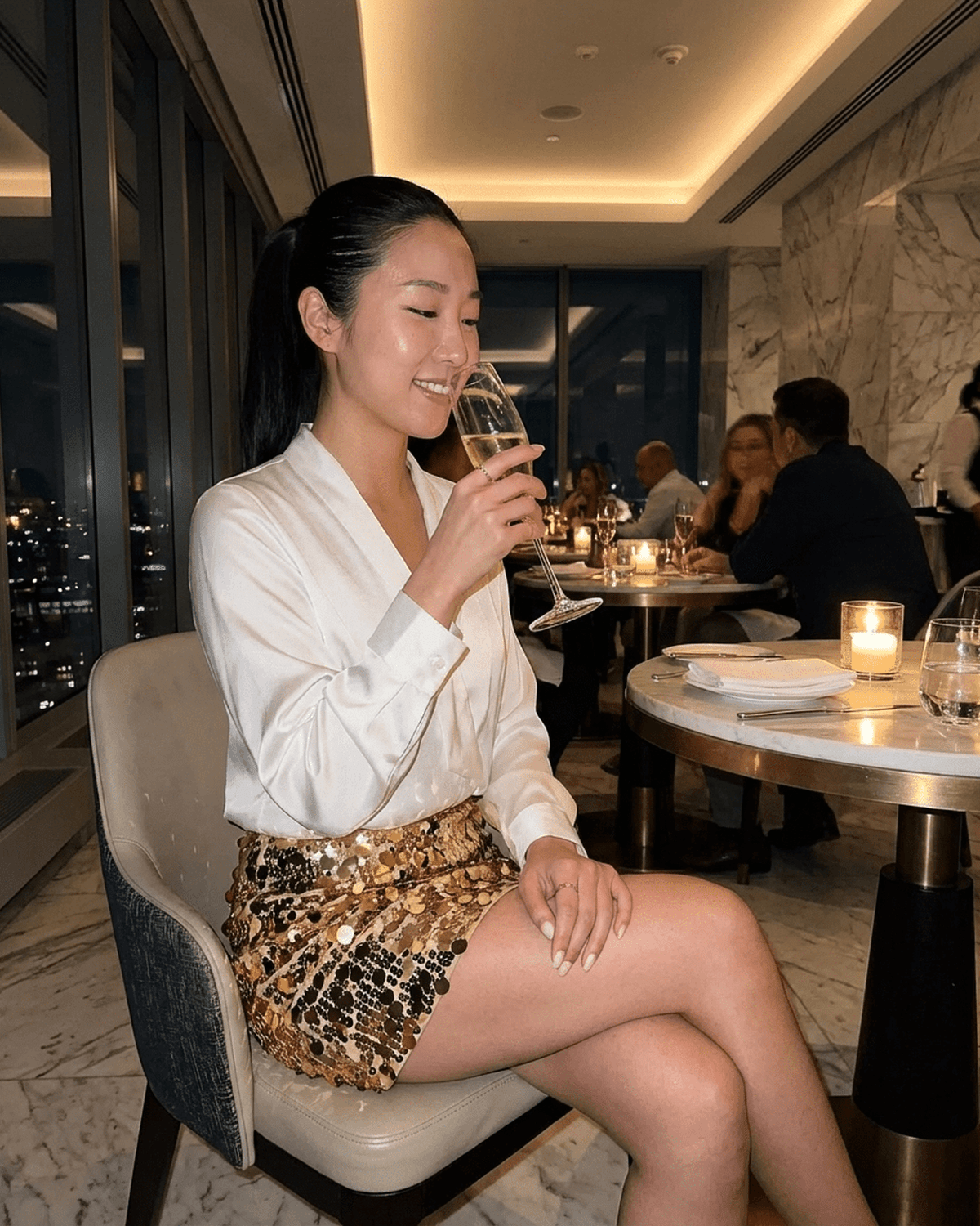 Aurelia Mini Skirt by SLIMONA worn by a woman enjoying a drink in a stylish restaurant, showcasing its bold sequin design.