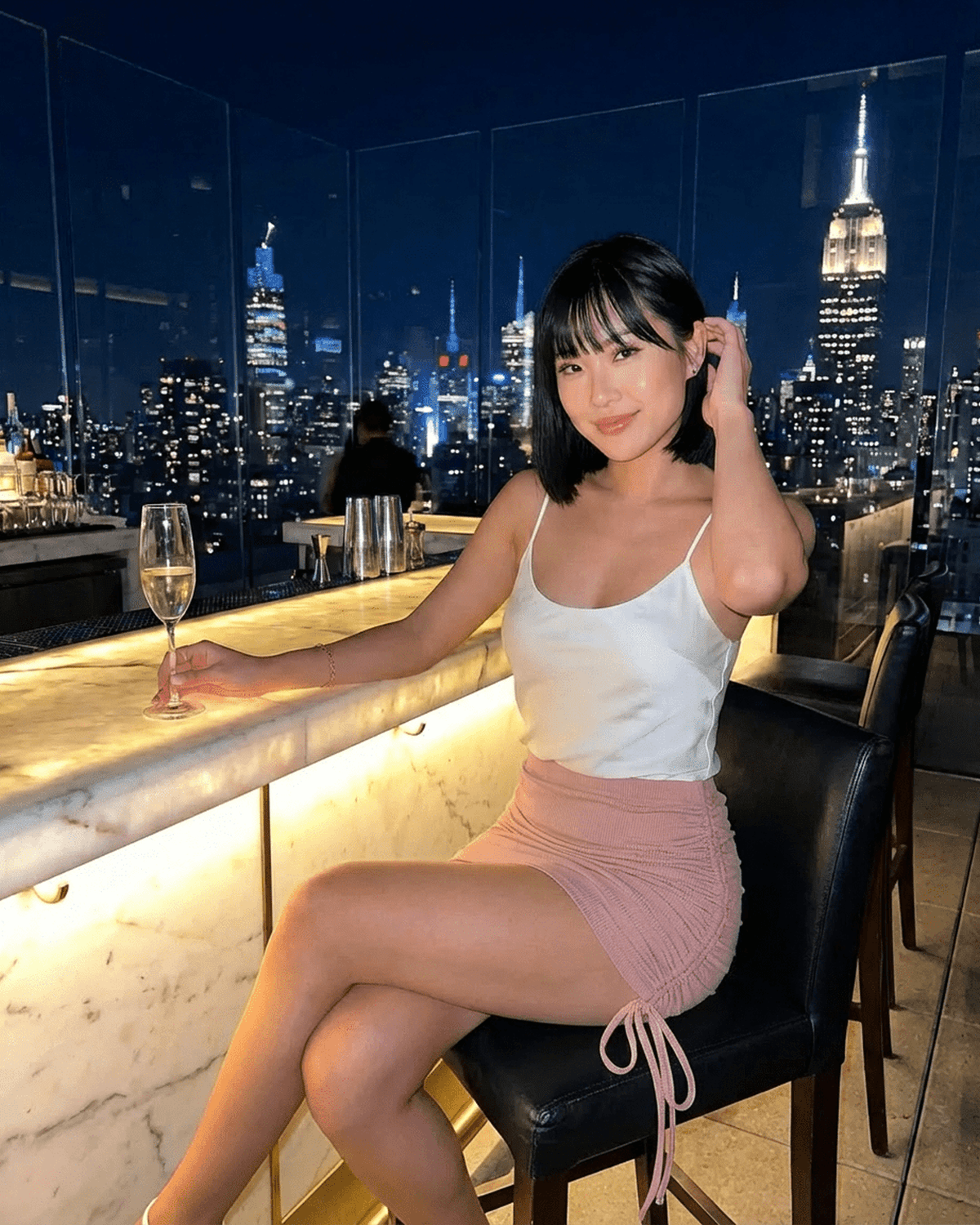 Model wearing Blush Mini Skirt by SLIMONA at rooftop bar with city skyline at night.