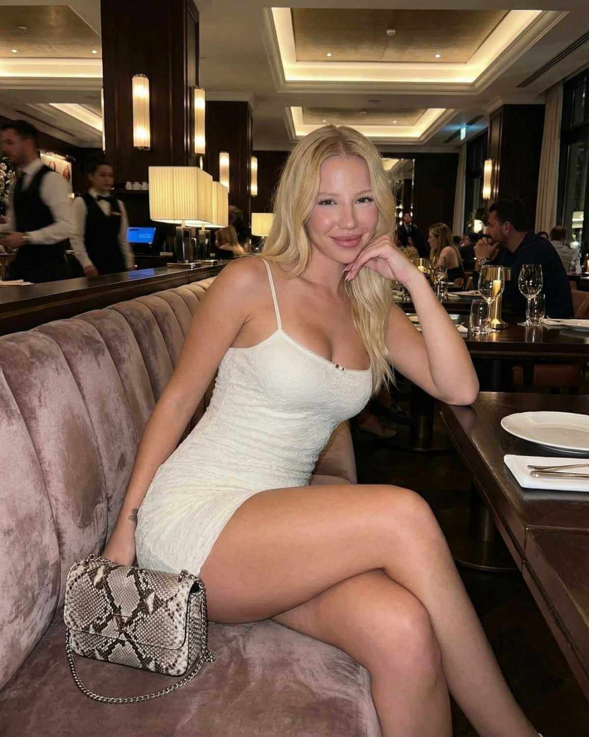 Model wearing Elara Mini Dress by SLIMONA, showcasing elegant lace bodycon design in a modern dining setting.