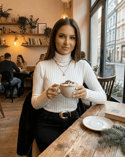 Woman wearing Elara Sweater, enjoying a cozy coffee in a stylish café setting.