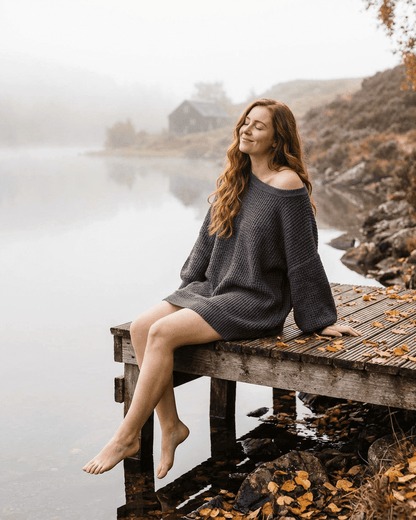 Model wearing Ember Mini Dress by SLIMONA, enjoying a serene lakeside view in a deep charcoal ribbed knit.