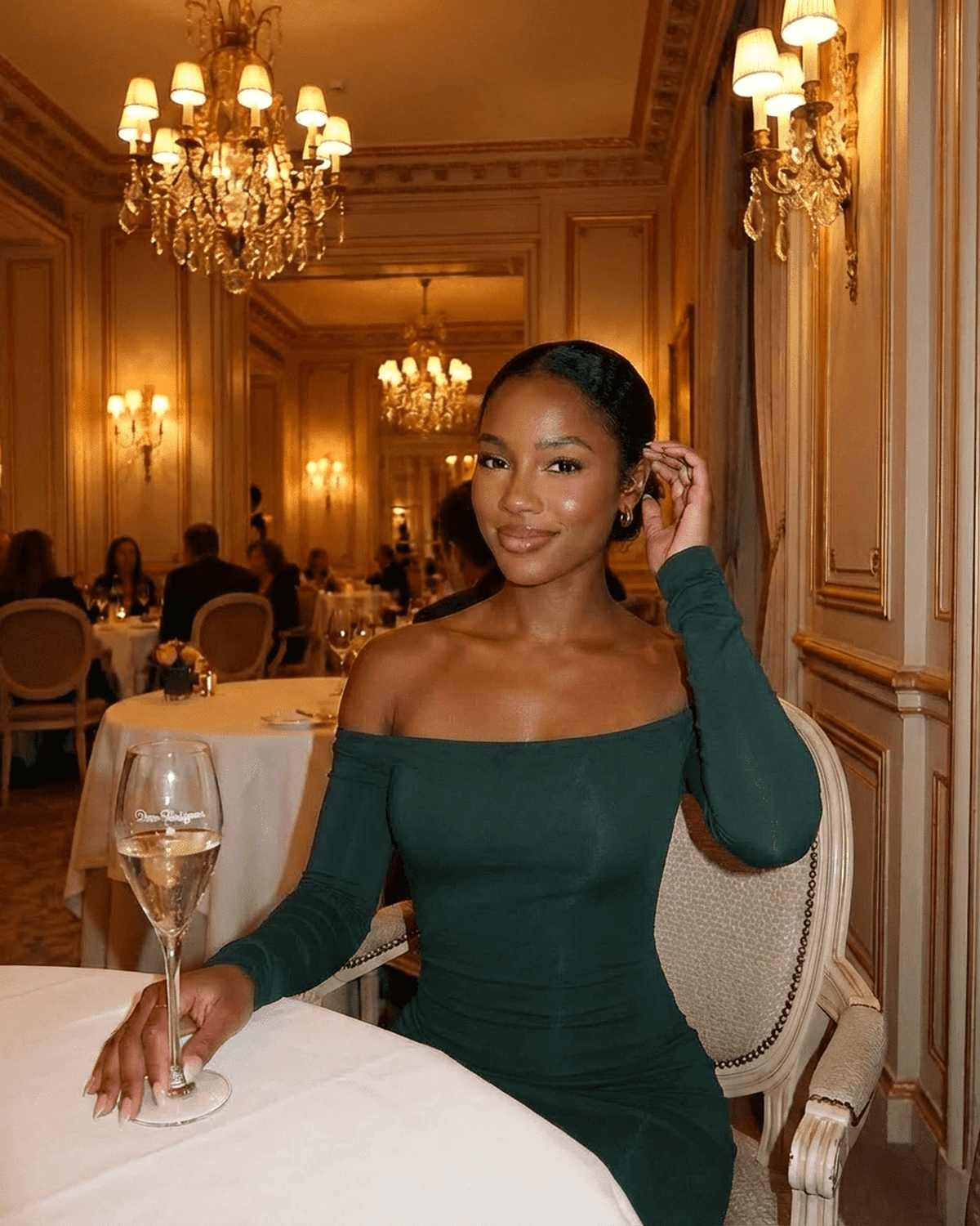 Elegant woman in an Emerald Maxi Dress by SLIMONA, enjoying a drink in a luxurious dining setting.