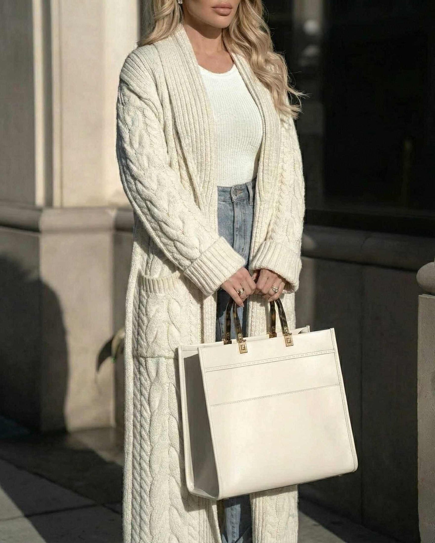 Model wearing the Milano Cardigan by Lauven, a long cable-knit wool blend layer, styled with a white top and chic bag.