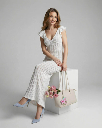 Model wearing Lauven Ivory Lace Maxi dress with ruffle sleeves, holding a bag and flowers.
