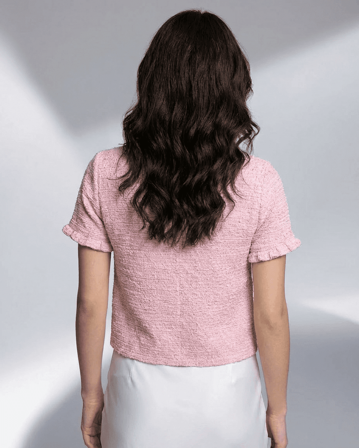 Back view of a woman wearing a pink Camellia Cardigan by SLIMONA, showcasing short sleeves and textured knit.