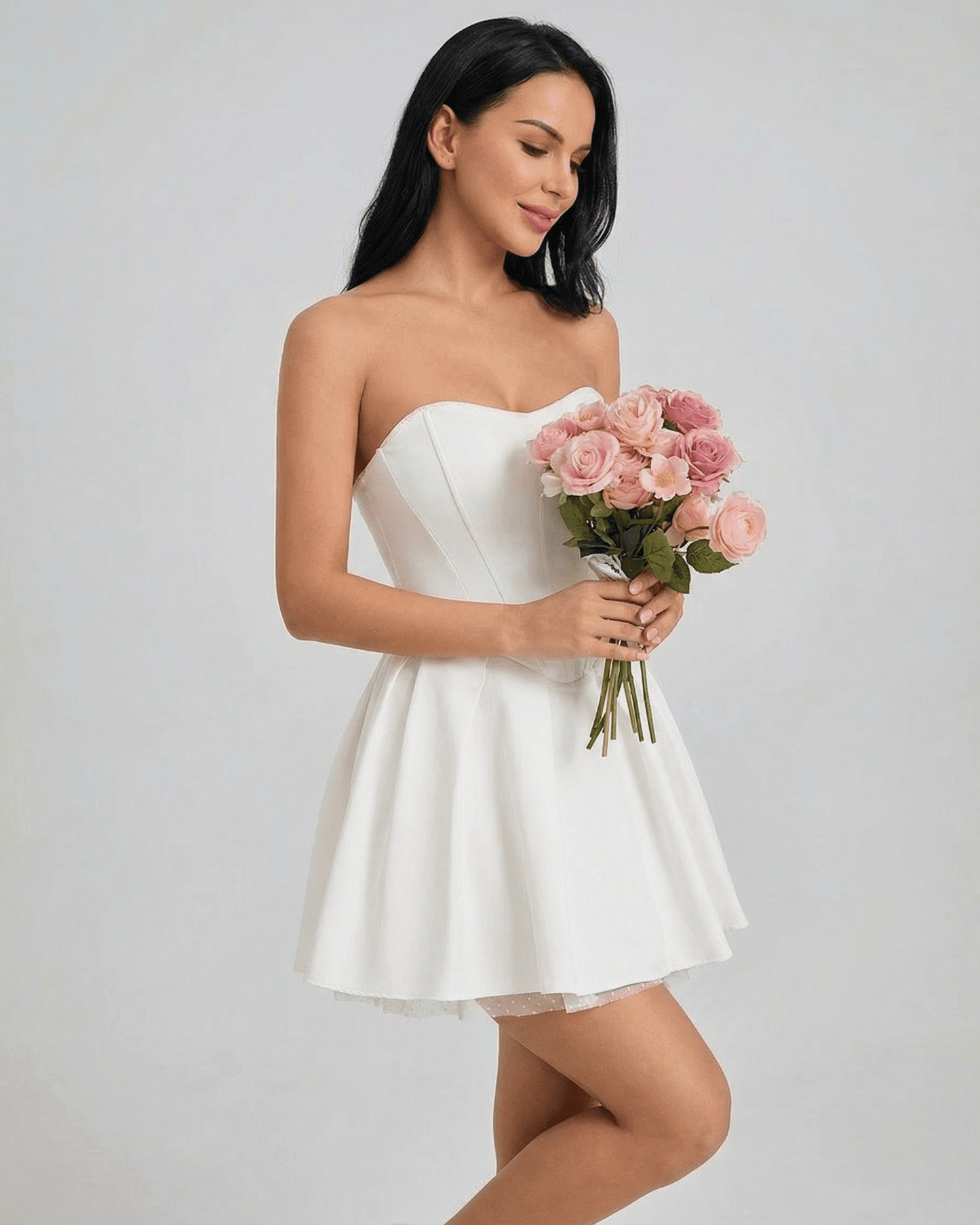 Model wearing the Celeste Mini Dress by SLIMONA, holding a bouquet of pink roses in a serene pose.