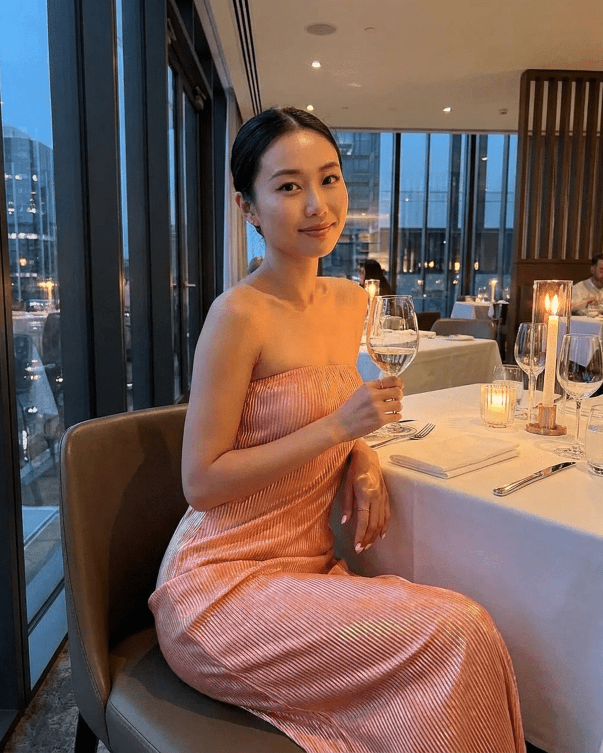 Woman wearing a Champagne Maxi Dress by SLIMONA, seated at a restaurant holding a glass of wine.