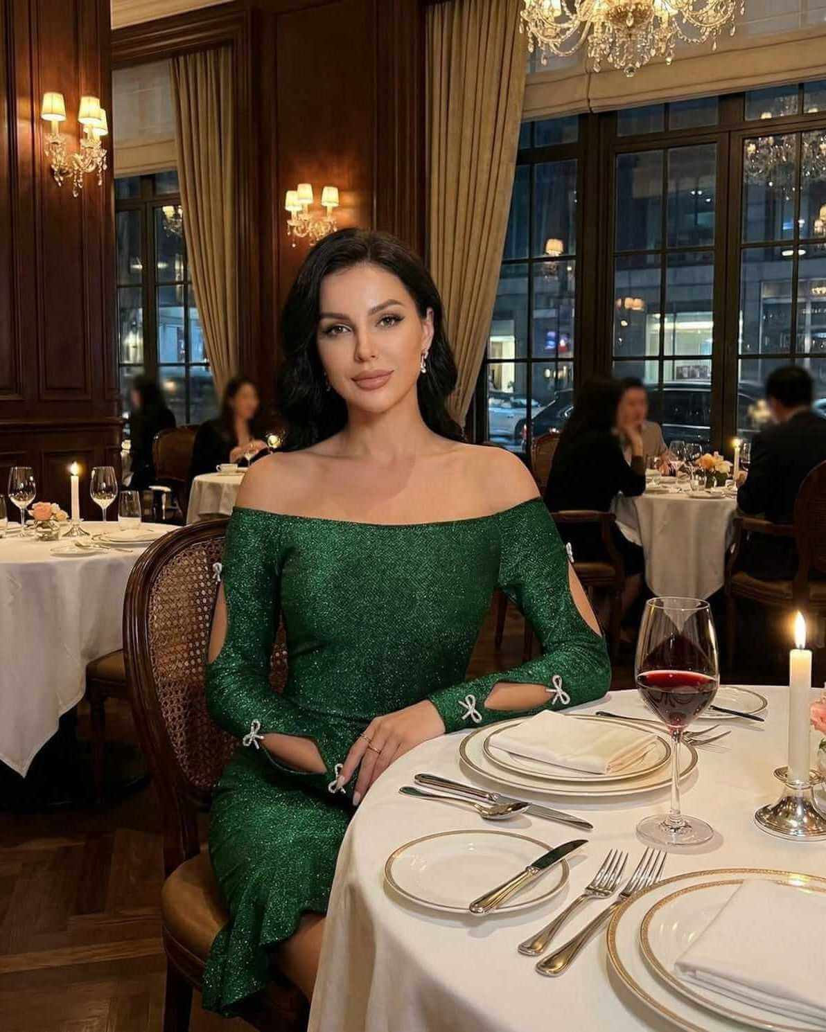 Elegant woman wearing an Emerald Mini Dress by Lauven, off-the-shoulder bodycon style with cutouts, sitting in a fine dining setting.
