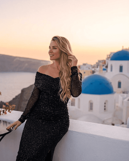 Elegant Noir Maxi Dress by SLIMONA, showcasing off-the-shoulder style and sheer mesh sleeves in a scenic sunset setting.