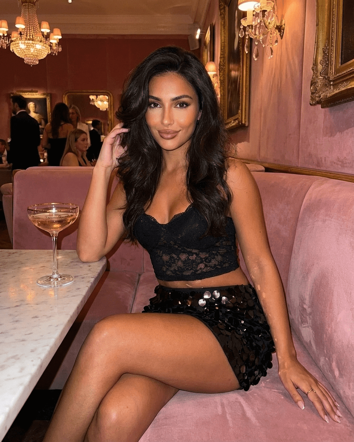 A woman wearing the Obsidian Mini Skirt with black sequin hem, seated elegantly at a table, showcasing SLIMONA fashion.