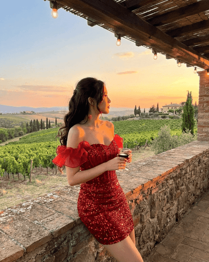 Scarlett Mini Dress by SLIMONA, red sequin off-the-shoulder bodycon with ruffle detail, outdoors at sunset.