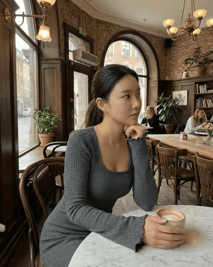 Woman in a coffee shop wearing a Slate Maxi Dress, ribbed knit with a square neckline, enjoying a warm drink.