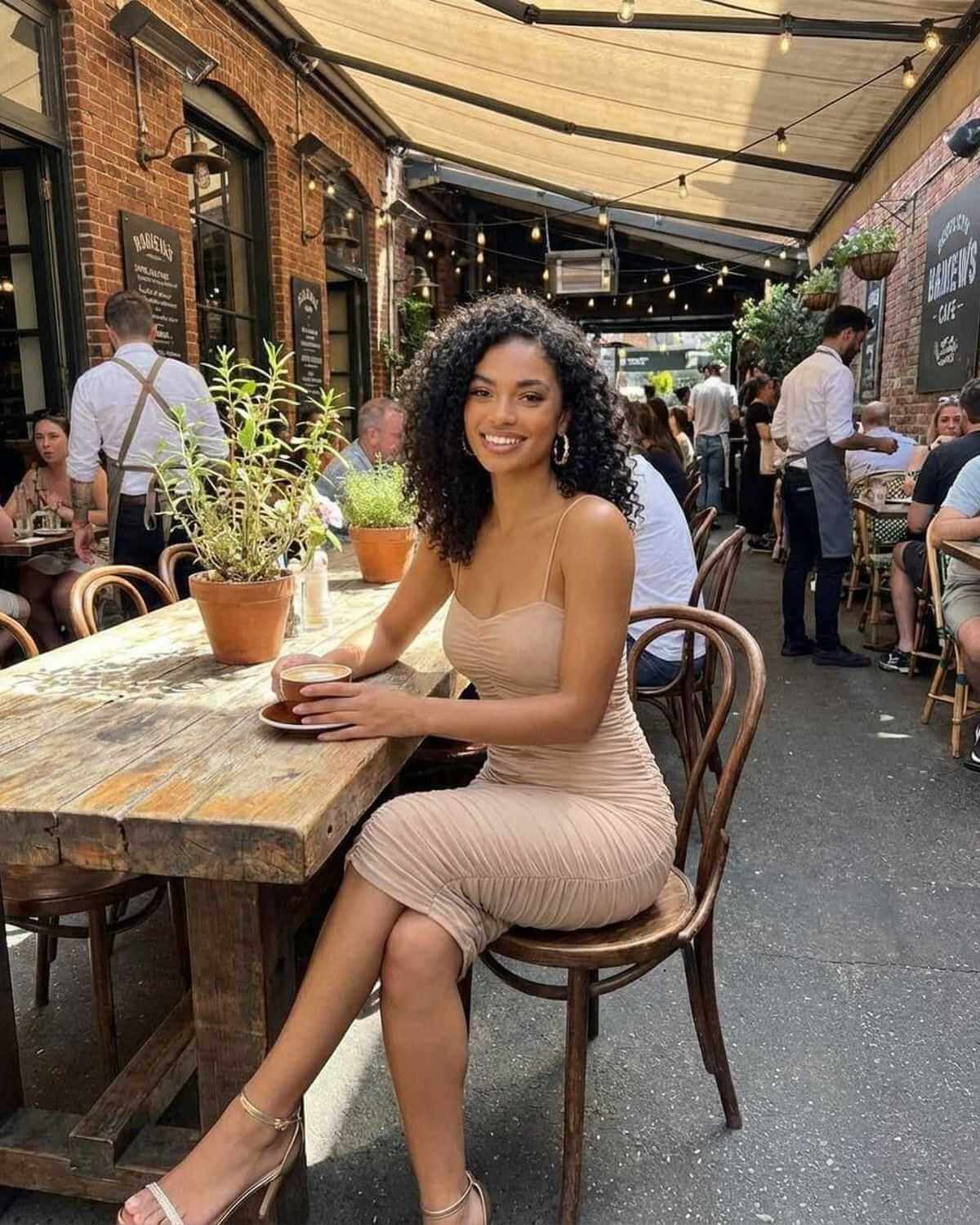 Woman wearing Solenne Midi Dress by SLIMONA, sitting at a cafe table in a chic outdoor setting.