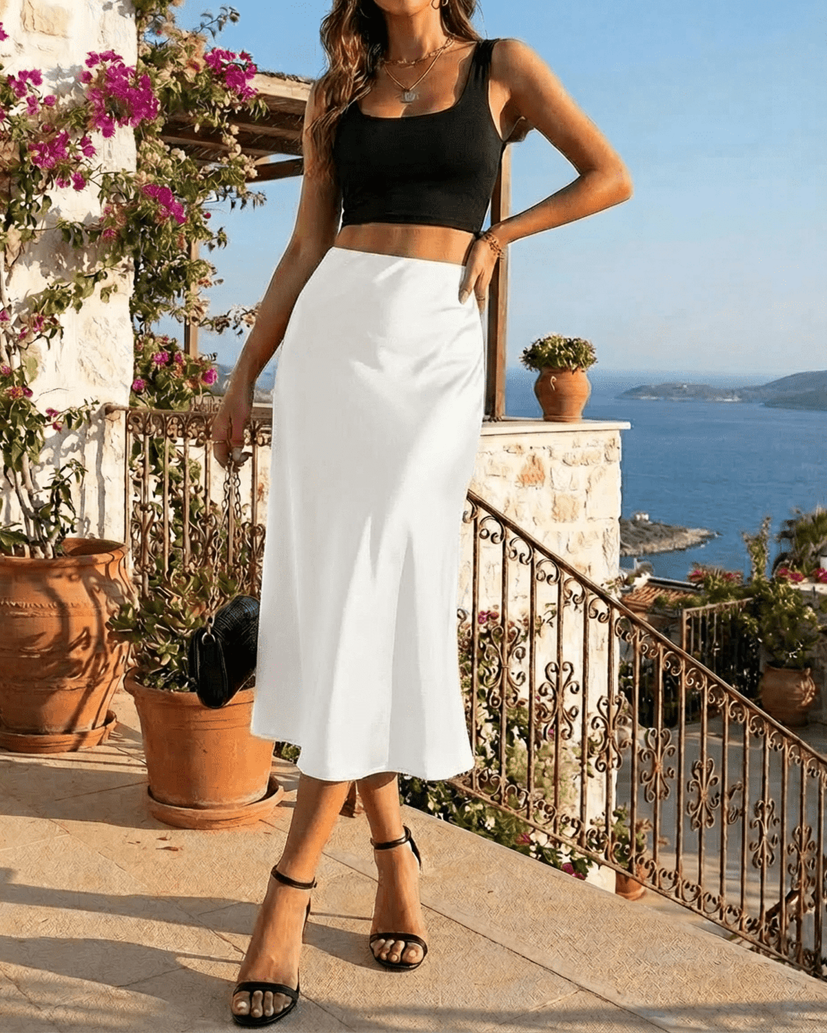 Model wearing the Luna Midi Skirt by SLIMONA, a satin mermaid skirt, with a stunning seaside view in the background.