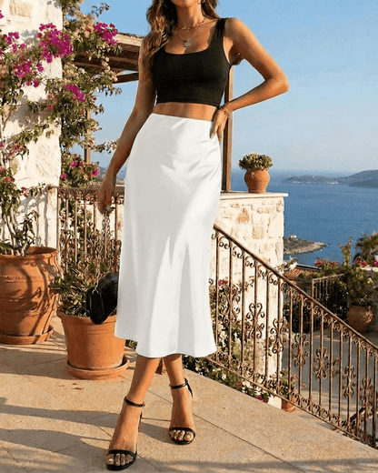 Model wearing the Luna Midi Skirt by SLIMONA, a satin mermaid skirt, with a stunning seaside view in the background.