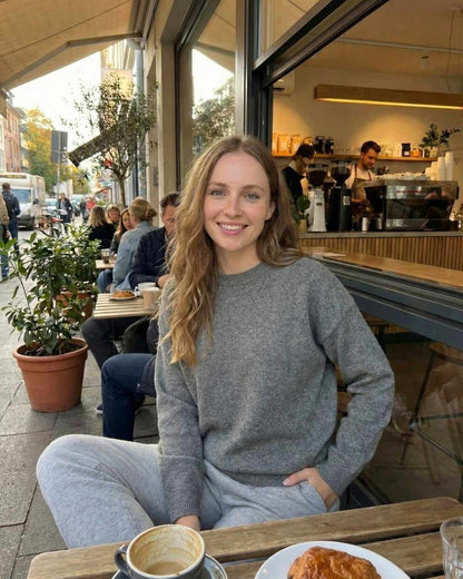 Woman wearing Lyra Pullover by SLIMONA, enjoying coffee at a cafe with friends, showcasing relaxed fit and modern style.