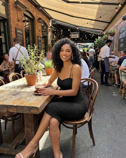 Woman in Noctyra Midi Dress by SLIMONA sitting at a cafe table, showcasing its elegant silhouette and chic design.