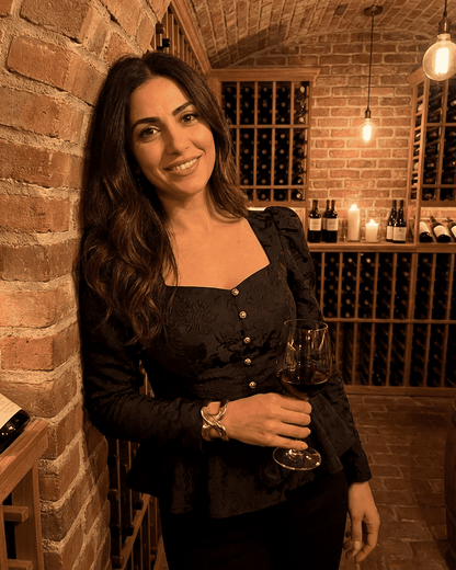 Woman wearing a Noir Corset Top by SLIMONA, holding a glass of wine in a wine cellar.
