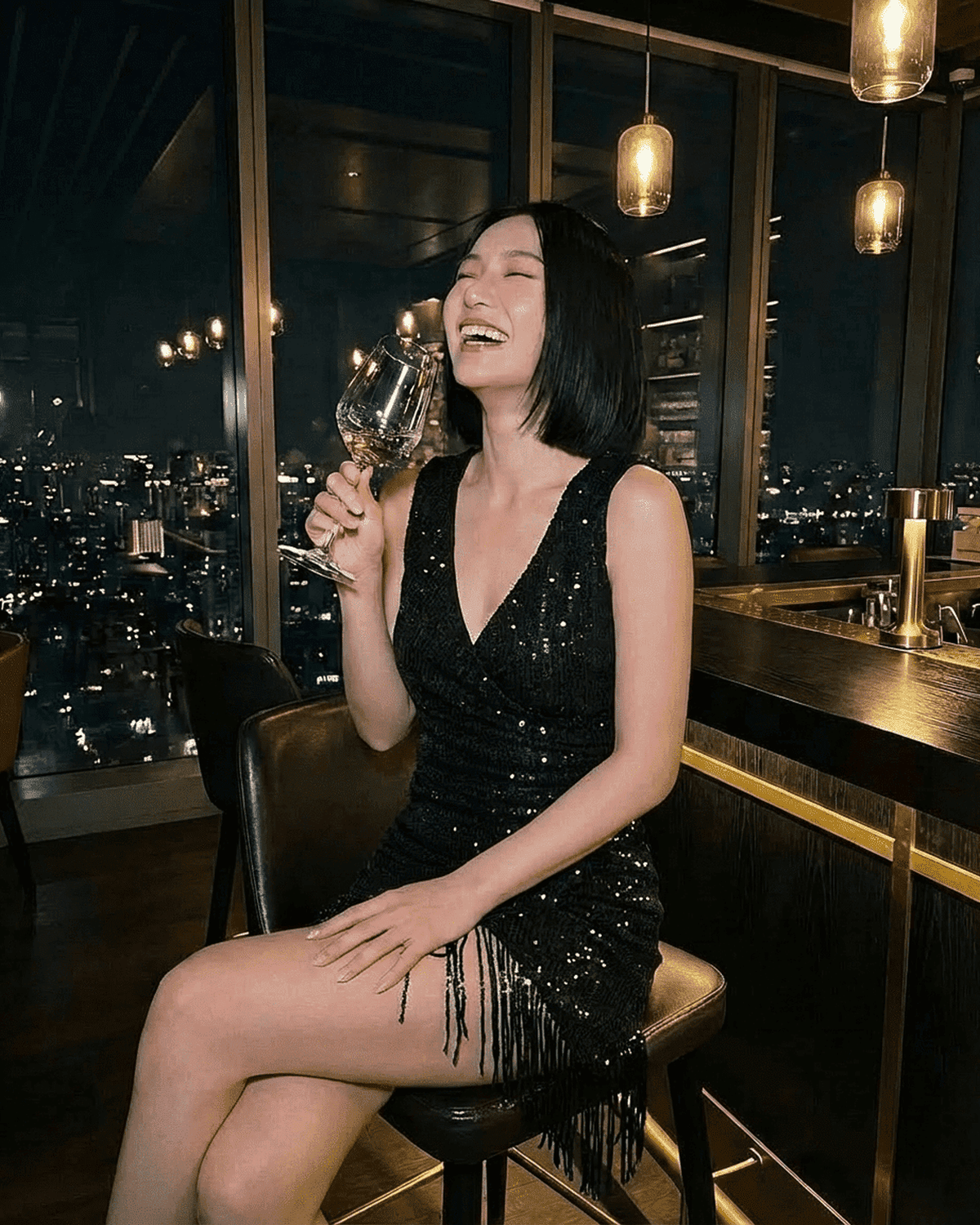 Woman laughing in the Noir Mini Dress by SLIMONA, featuring black sequins and a fringe hem, perfect for glamorous evenings.