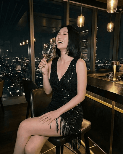 Woman laughing in the Noir Mini Dress by SLIMONA, featuring black sequins and a fringe hem, perfect for glamorous evenings.