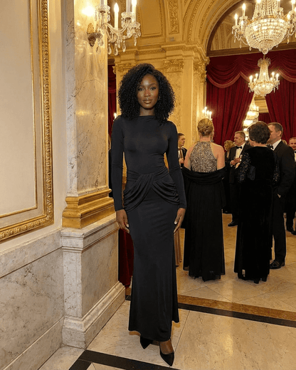 Model wearing Orion Maxi Dress by SLIMONA, showcasing long sleeve design and ruched waist detail in elegant setting.