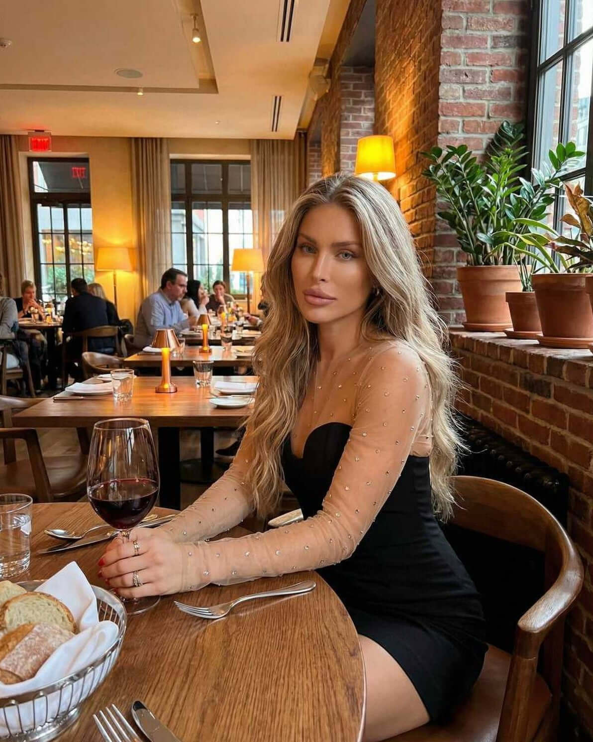 Stylish woman wearing Stella Mini Dress by Lauven with sheer embellished sleeves in a chic restaurant setting.