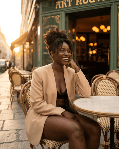 Savona Blazer by SLIMONA worn by a smiling woman in a chic café setting, showcasing modern elegance.