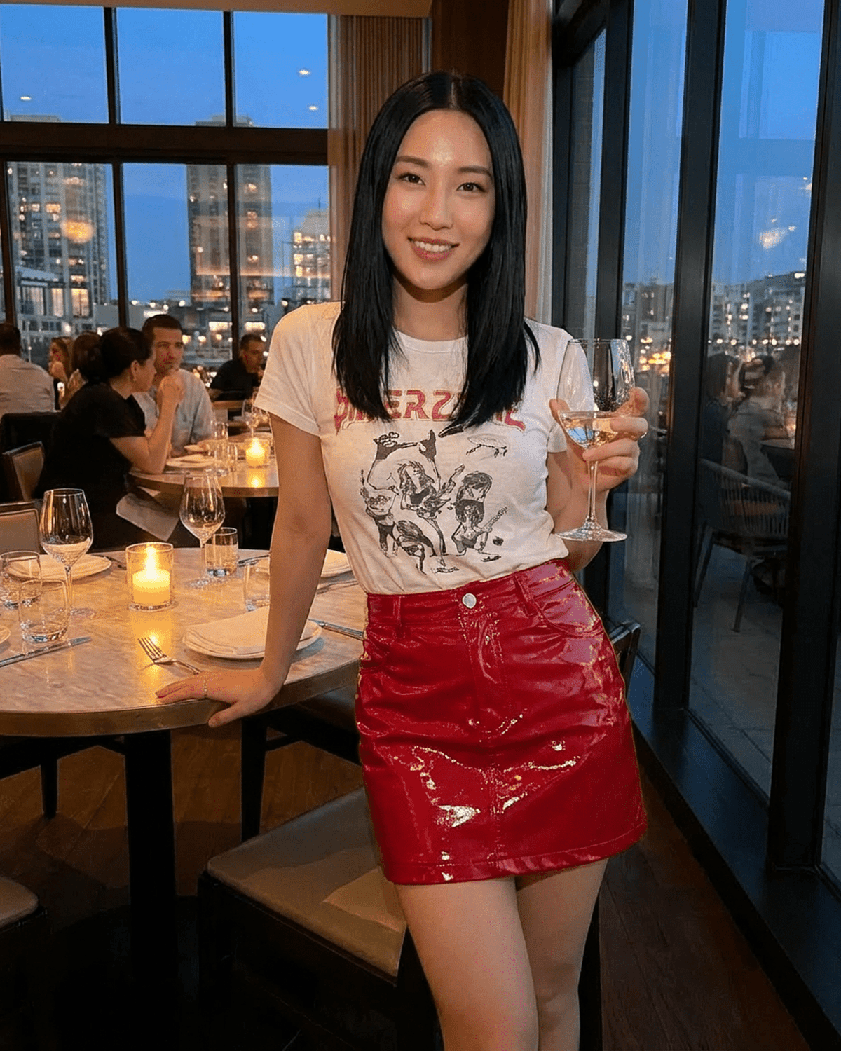Woman wearing a Crimson Mini Skirt by SLIMONA while holding a glass in a stylish restaurant setting.