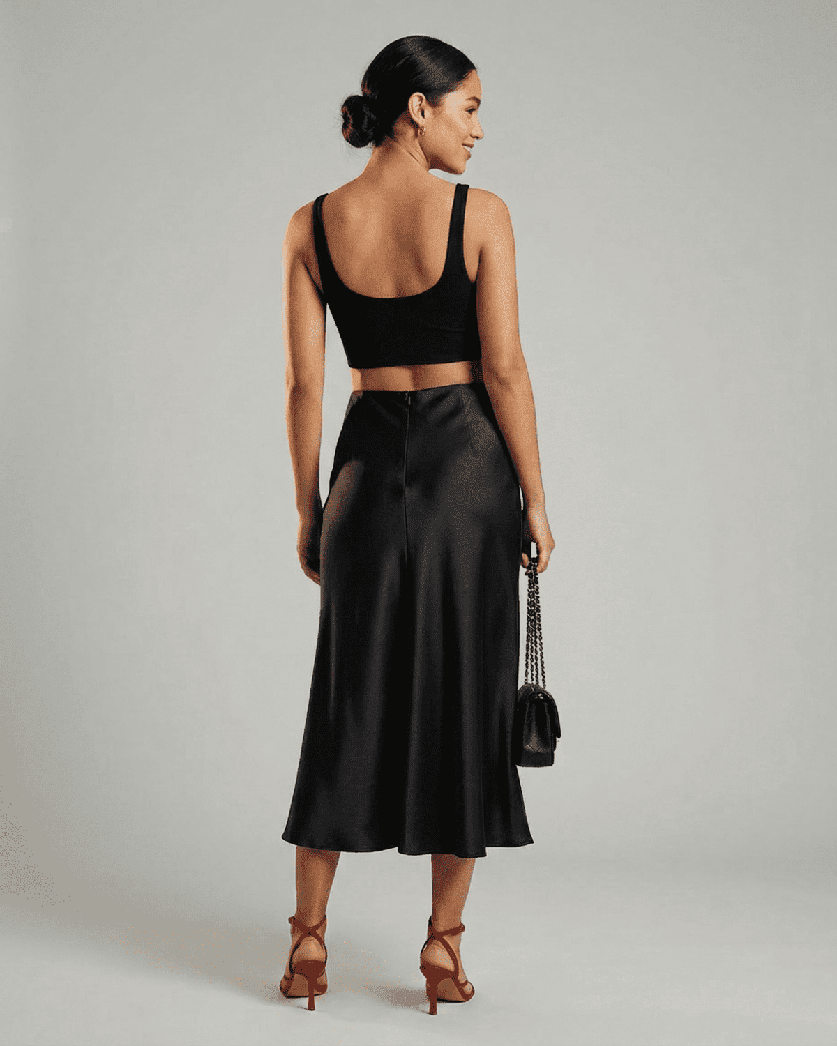 Back view of a model wearing the Noirelle Midi Skirt by SLIMONA, showcasing its satin mermaid hem.