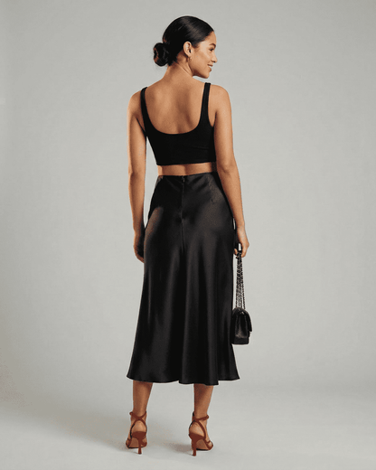 Back view of a model wearing the Noirelle Midi Skirt by SLIMONA, showcasing its satin mermaid hem.