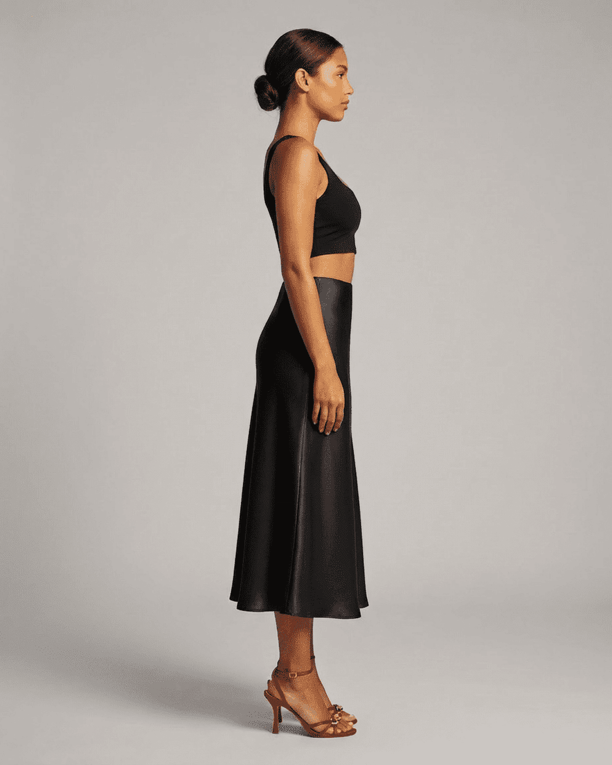 Model showcasing Noirelle Midi Skirt from SLIMONA in sleek black satin, highlighting its mermaid silhouette.