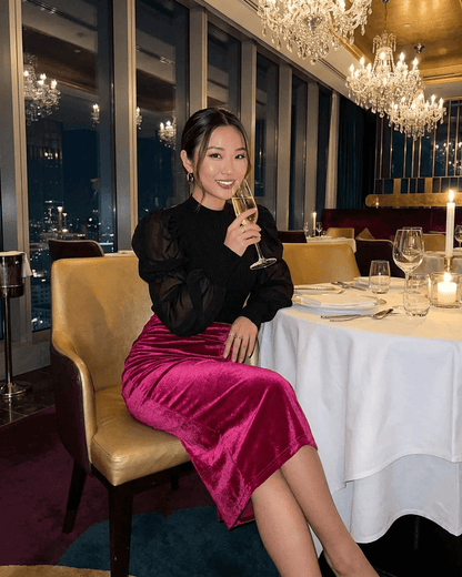 Elegant woman in Rosalia Midi Skirt, high-waisted velvet pencil style, at a chic restaurant setting.