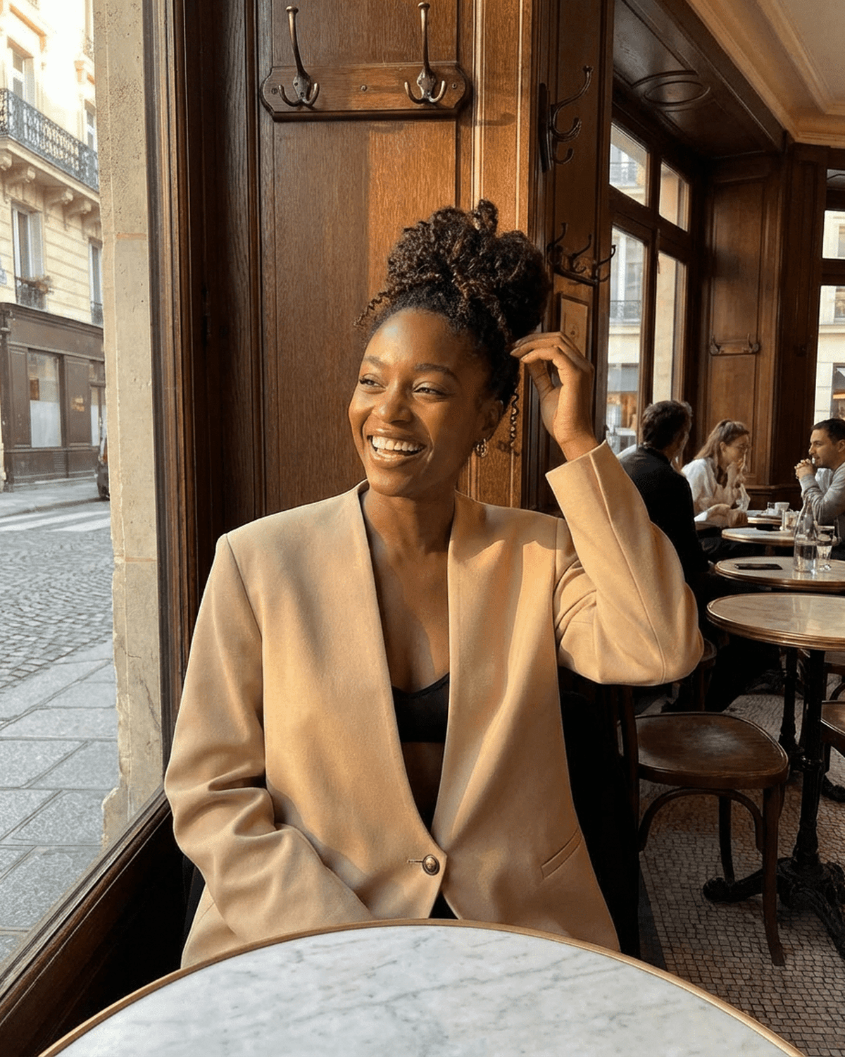 Woman wearing Savona Blazer by SLIMONA, showcasing a modern beige tailored look in a stylish café.