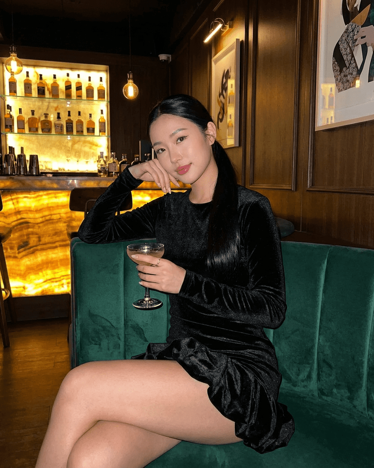 Velora Mini dress from SLIMONA in black velvet worn by a woman enjoying a cocktail in a stylish bar setting.