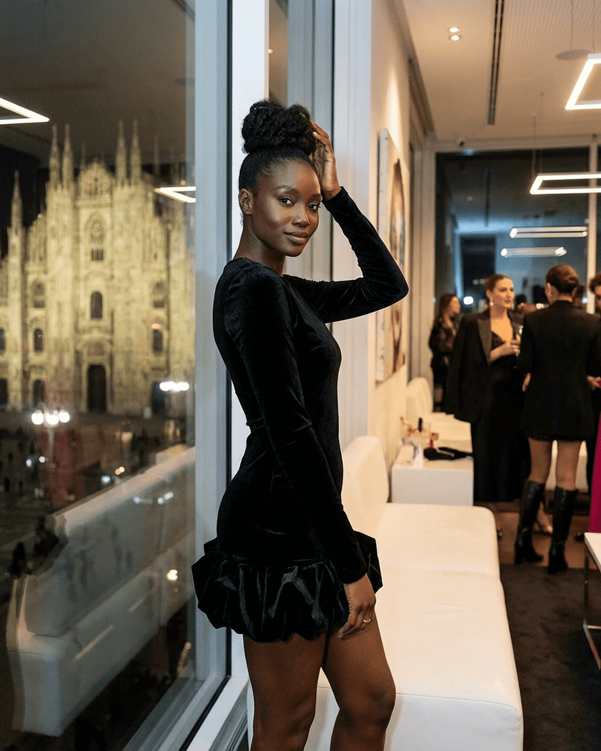 Model wearing Velora Mini Dress Black by SLIMONA, featuring luxe velvet and pleated hem, standing in urban setting.