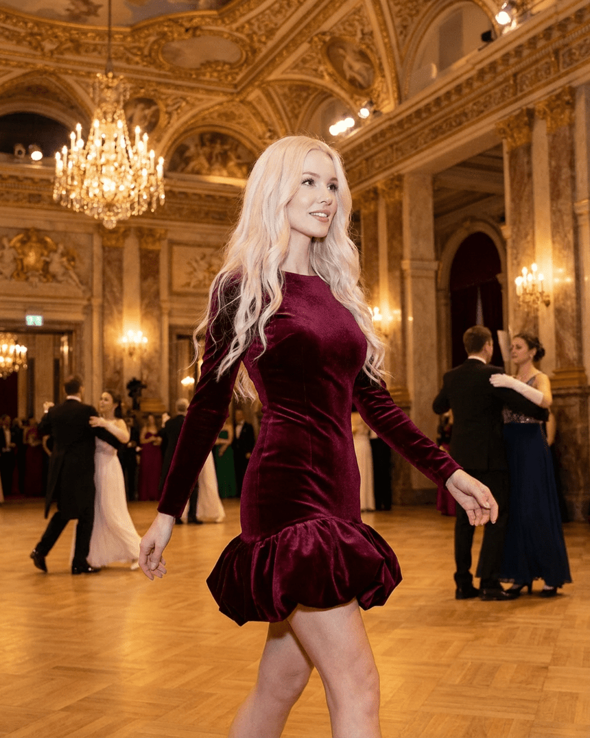 Stylish woman wearing Velora Mini Dress by SLIMONA, showcasing luxe velvet and a pleated hem in a grand ballroom setting.